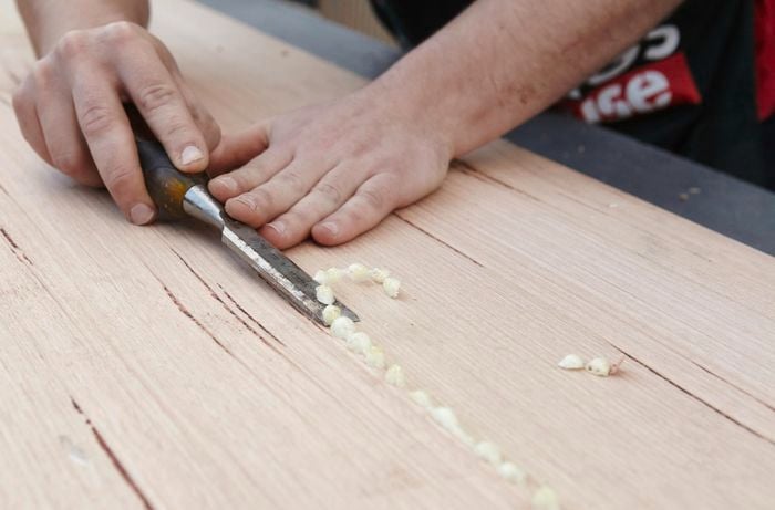 A person using a chisel to remove dried glue from a join in timber