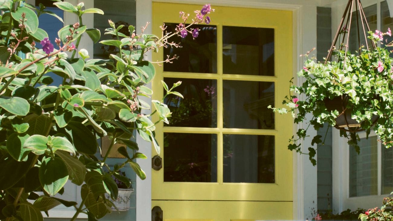 A bright yellow front door surrounded by lush green foliage and flowering plants