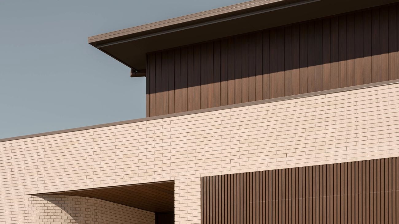 Close-up of a modern home facade with warm brown vertical timber cladding above light cream brickwork, featuring a deep roof eave casting strong shadow lines.