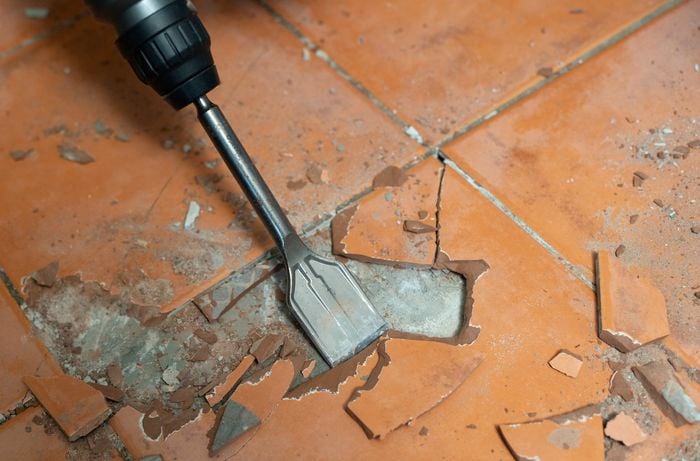 A person is using a rotary hammer with a chisel bit to break apart tiles during tile removal.