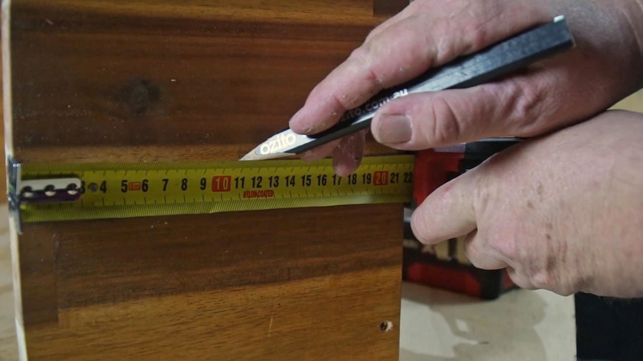 Hands holding a pencil and measuring tape to mark handle holes on timber