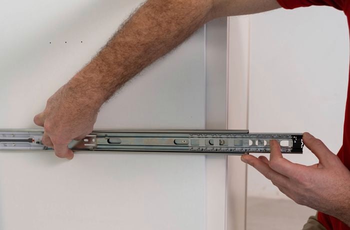 A person is laying out the drawer runners and inspecting the cabinet interior. 