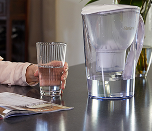Person holding a glass of water next to a water filter jug
