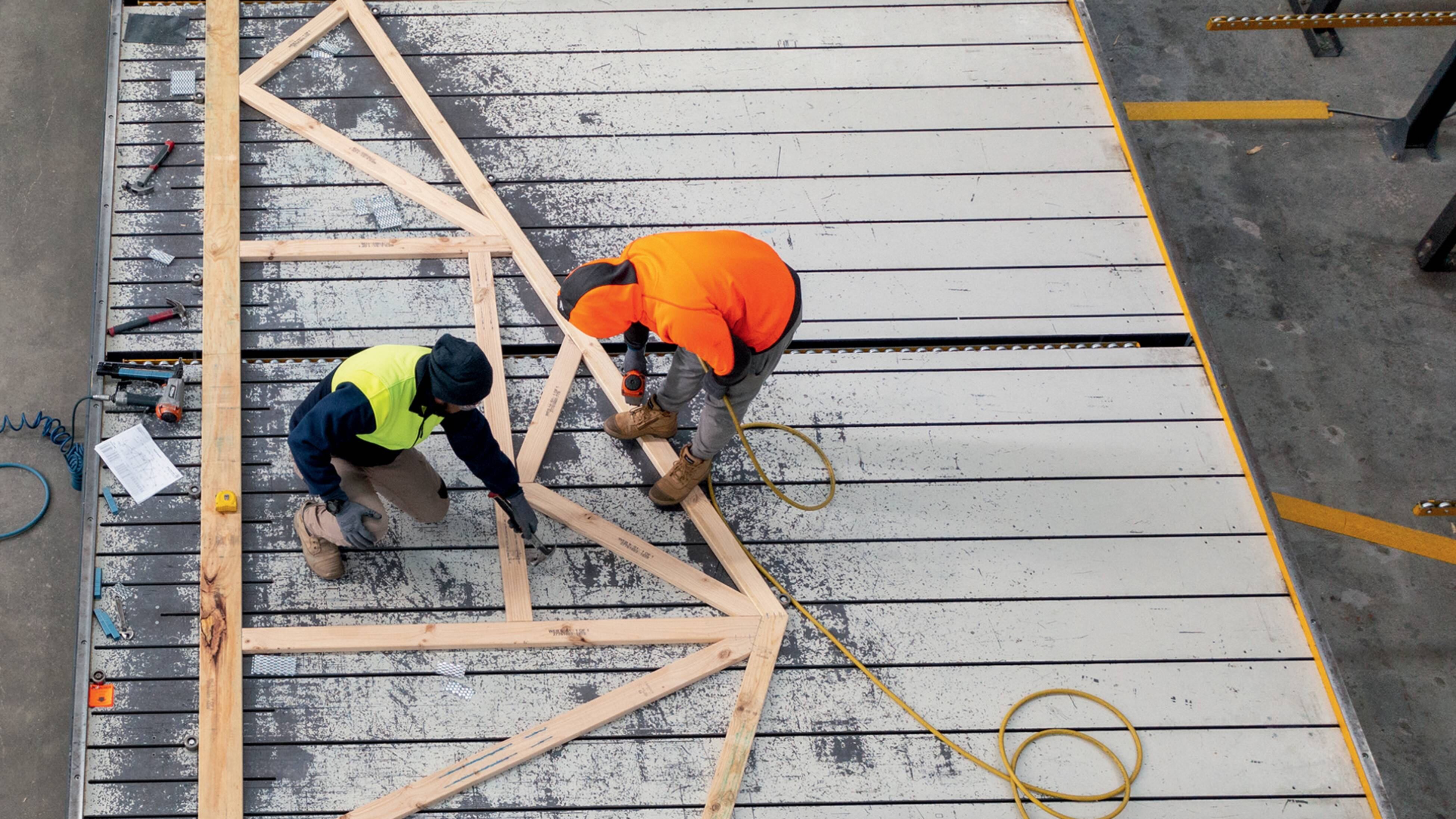 Two men in hi-vis work on Bunnings Trade frame and truss at a plant