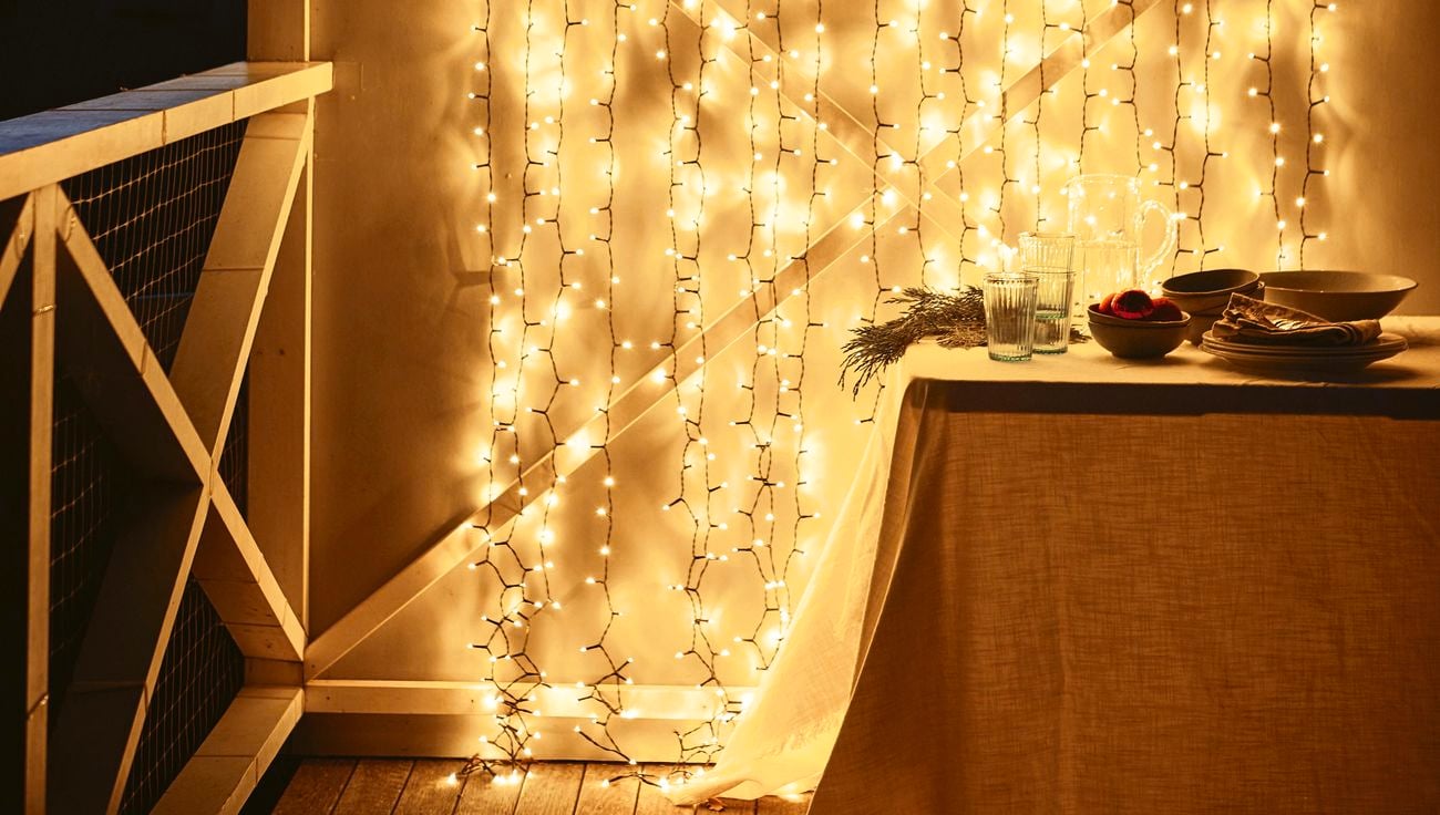 A string of fairy lights glowing against a white wall on a deck at night