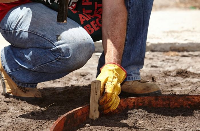 Bunnings team member hammering a peg into the curved edging of a path yet to be filled with concrete.