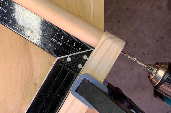 A hole being drilled into a length of dowel secured to another length of timber, squared against a square rule