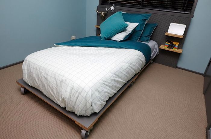 A completed wooden bed frame on wheels, with a made bed in a teal themed bedroom