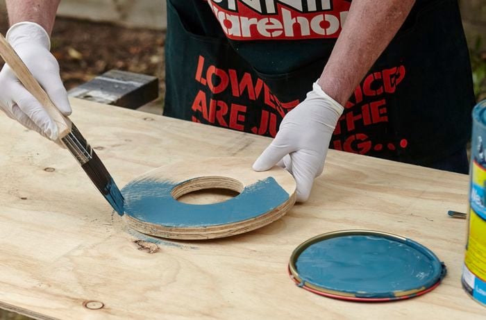 A person painting a piece of plywood in the shape on a circle