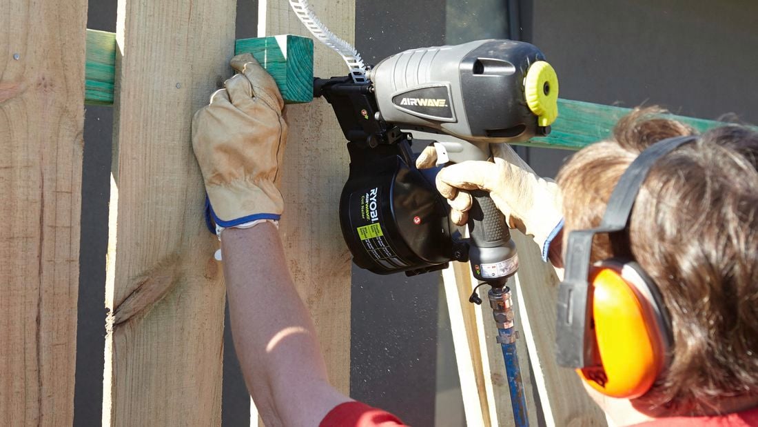 Person installing fence paling with nail gun.