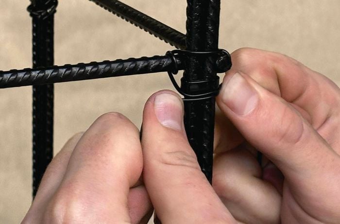 A pair of hands tie-wiring a vertical vegetable garden frame.
