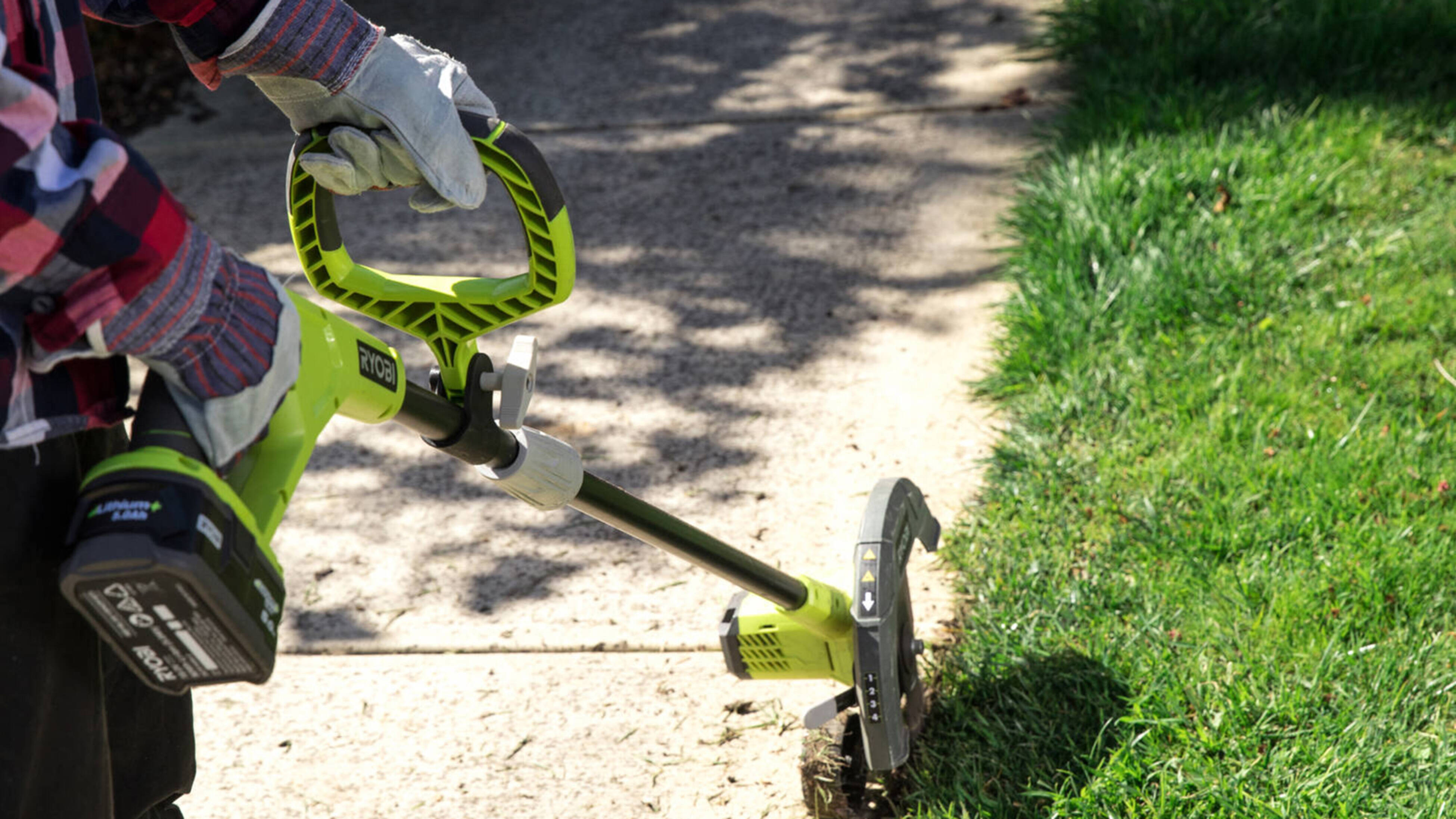 A person using a cordless lawn edger along a concrete footpath.]