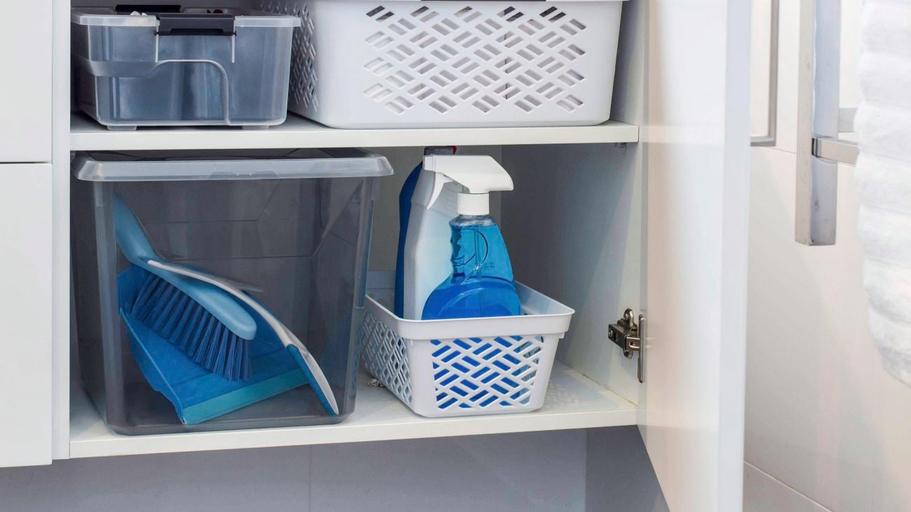Storage baskets and cleaning products in bathroom vanity unit cupboard.
