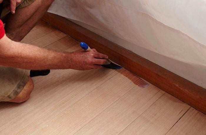 A person using a paintbrush to apply sealer around the edge of a hardwood floor