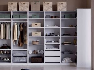 A large open wardrobe unit with shelves and hanging rails holding clothes, shoes, folded towels, storage boxes, wicker baskets, drawers and boxes on top. A floor lamp stands on the left.