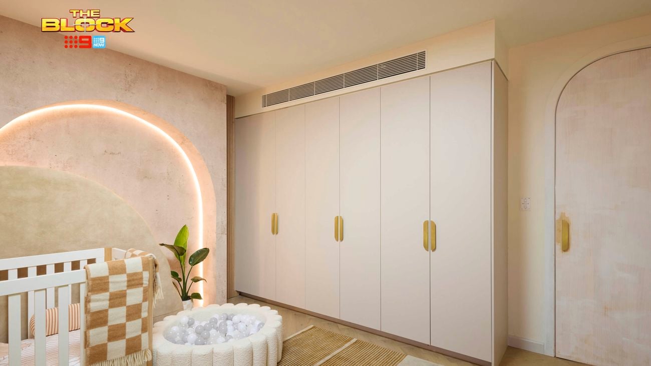Neutral baby bedroom with brown and tan colours. Showcasing a cot and small ball pit in front of an arched feature wall with feature lighting. There is a wardrobe on the opposite wall.