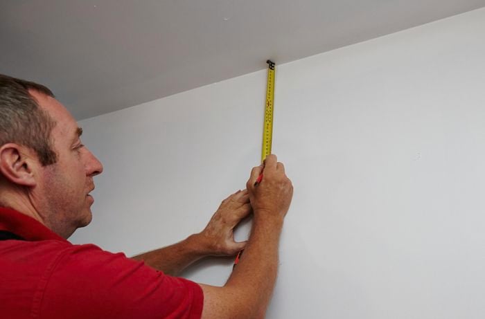 Heights for wire frame shelves being marked out on the wall of a walk in wardrobe by a Bunnings team member using a tape measure and pencil