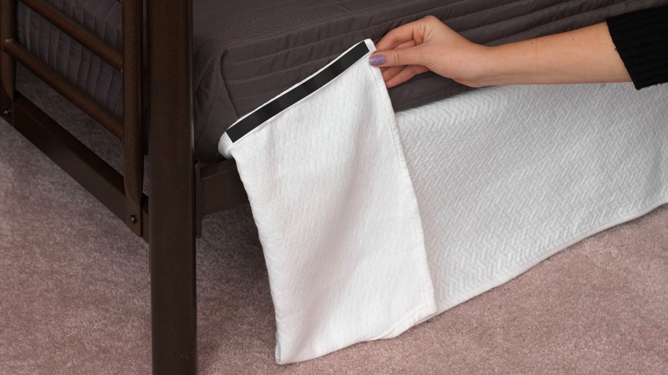 Hand holds a white strip of fabric attached to the underneath of a bed with VELCRO®