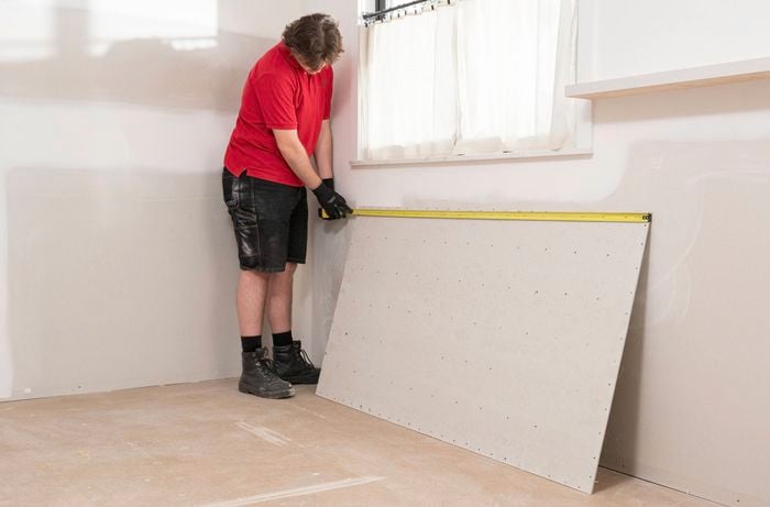 A Bunnings Team Member is measuring the size of an underlay sheet using a tape measure for accurate cutting.