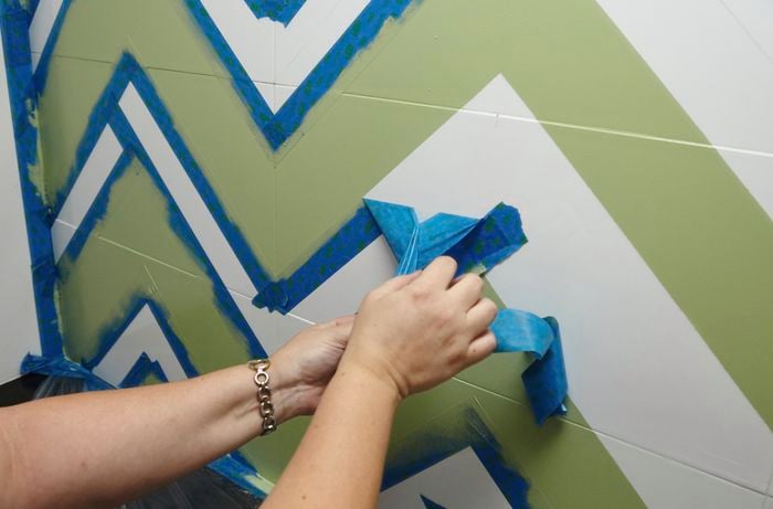 A person removing masking tape from splashback tiles