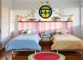 Two single beds in a Bluey-inspired bedroom with a watermelon rug, stained glass window, lanterns and pink bedhead panelling