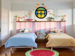 Two single beds in a Bluey-inspired bedroom with a watermelon rug, stained glass window, lanterns and pink bedhead panelling