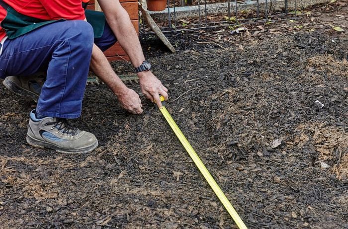 Person kneeling in bark mulch with measuring tape