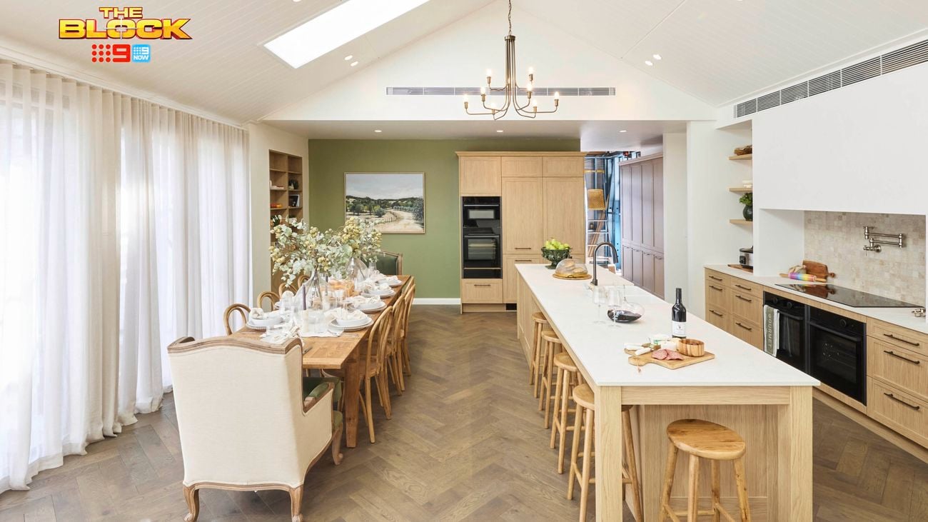 Kitchen with long island, wooden stools, and dining table by large windows.