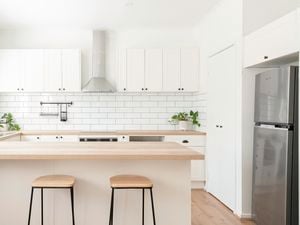 A kitchen with a timber benchtop, white cabinets and a white tiled splashback.