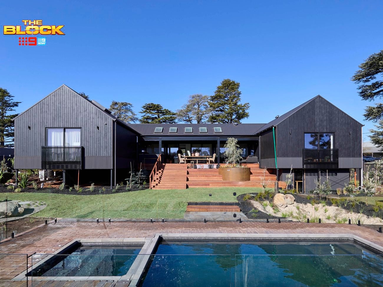 The back of a house with a pool in it, a rocked area, timber decking and many plants in it.