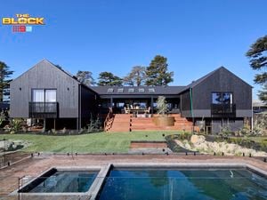 The back of a house with a pool in it, a rocked area, timber decking and many plants in it.