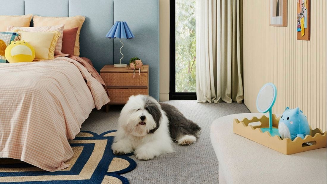 A bedroom with a dog next to the bed, a rug under the bed, and paintings in frames on the wall.