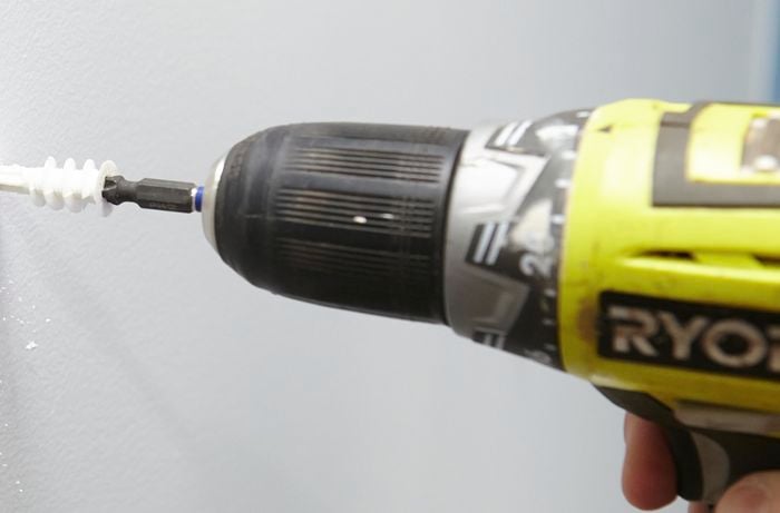 Close-up of a cordless driver screwing in a nylon wall anchor screw