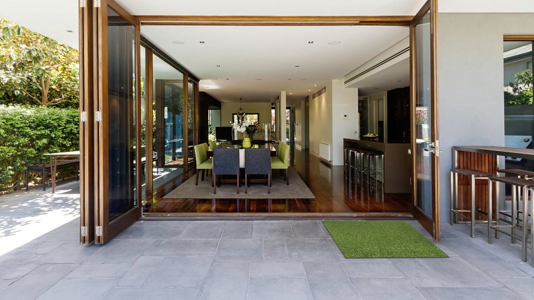 A matt of artificial turf sits outside the french doors of a house.