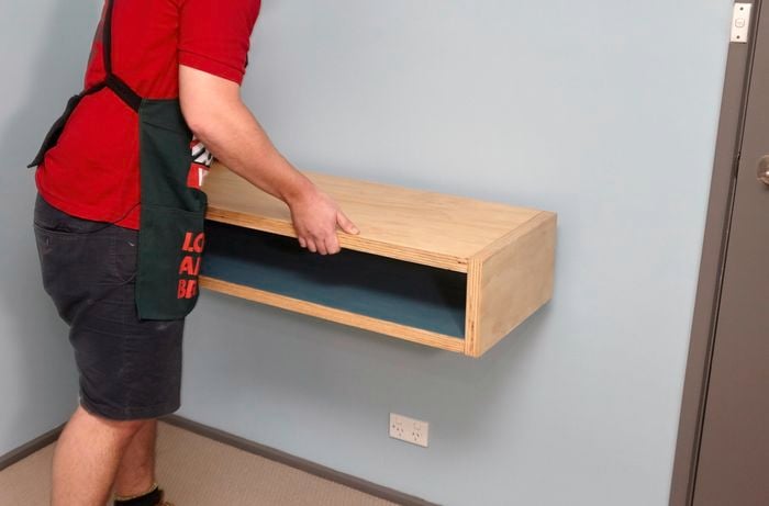 A person fitting a plywood box against a wall