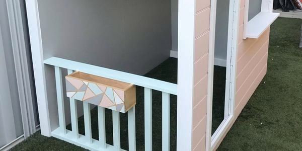 Pink painted cubbyhouse in a backyard with synthetic lawn