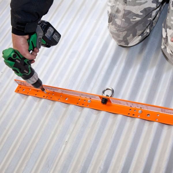 A person drilling a temporary roof anchor on corrugated roofing