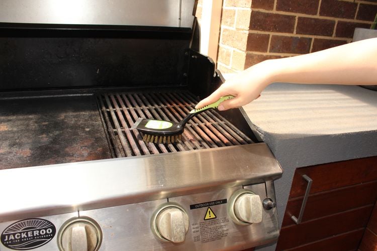 Person cleaning a BBQ with a steel scrubbing brush