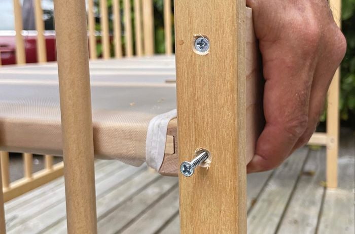 Close up of hand holding wooden cot with one nail drilled in and the other about to be drilled