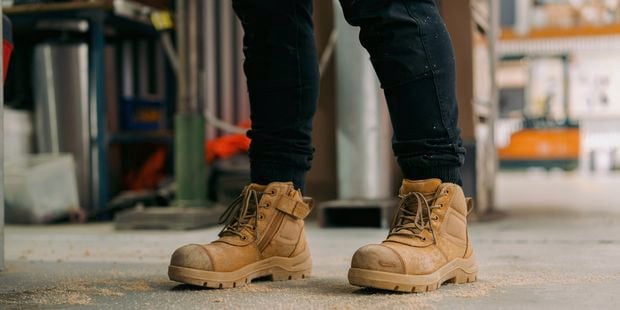 A person with work boots on standing in a construction site.