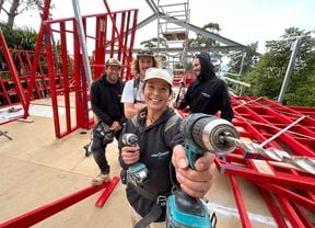 A female apprentice holds up a drill to the camera while three colleagues are behind her on a building site