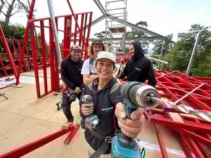 A female apprentice holds up a drill to the camera while three colleagues are behind her on a building site
