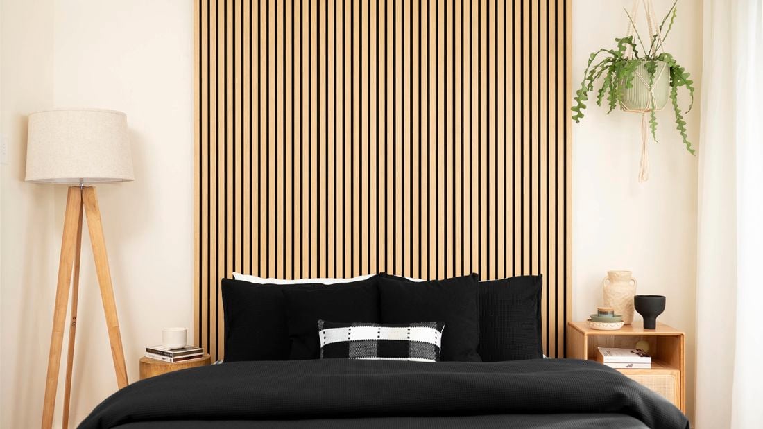 A room with floor lamp, bed and timber panels on the wall.