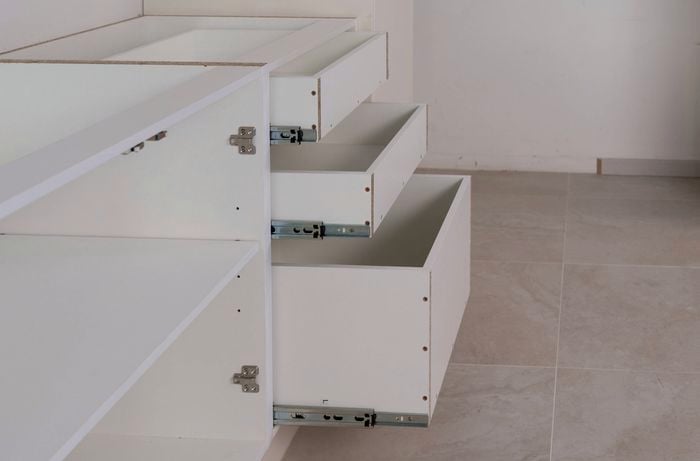 The image shows a partially assembled kitchen cabinet with three drawers fully extended on drawer runners.