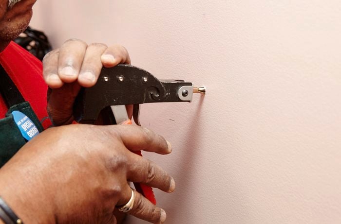 A person inserting anchors into a plaster wall using a wall anchor gun