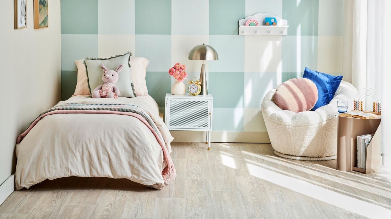 Child’s bedroom with bed in front of blue and white gingham feature wall, white fluffy bedside chair next to bed and a brass lamp on top of bedside table.