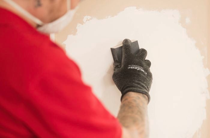 A person is using a sanding block to smooth the surface of the filled holes.