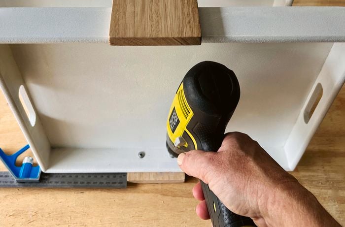 A person using a drill to secure button head screws in a MDF tray.