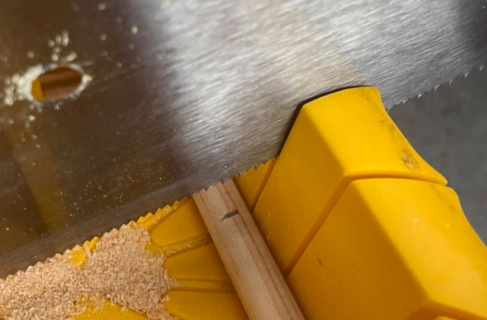 A person uses a saw to cut a piece of dowel.