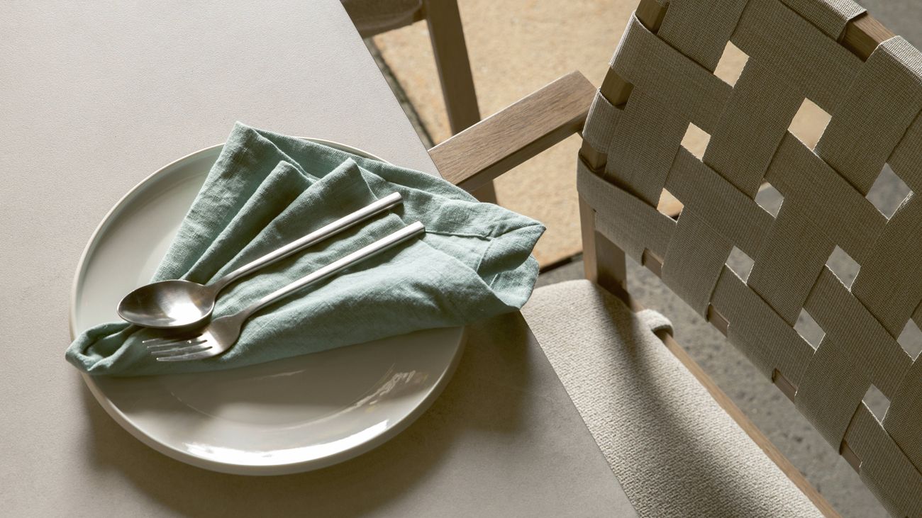 Place setting with plate, napkin, and cutlery on a table next to a chair.